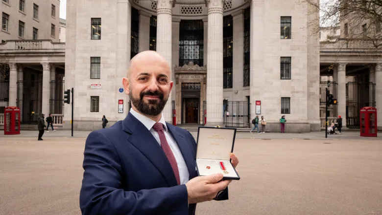 Paolo Aversa, stands in front of the Business School's main building, holding his Star of Italy medal in a case