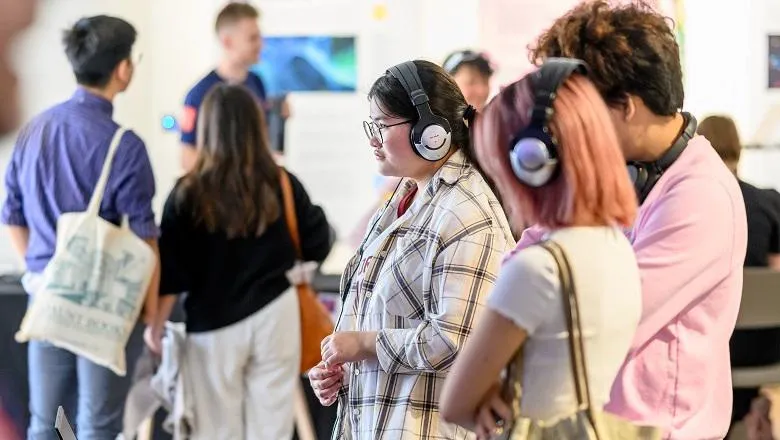 A side profile shot of two women wearing headphones. There are people in the background, out of focus.