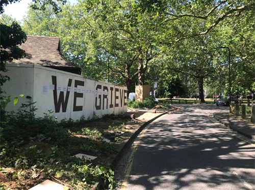 Picture of "WE GRIEVE" written on white hoarding in a park, taken at Clapton Common, Hackney