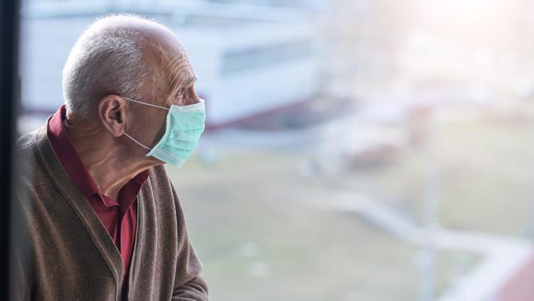 Older man wearing a face mask looking out a window