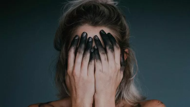 Woman covering face with ink stained hands