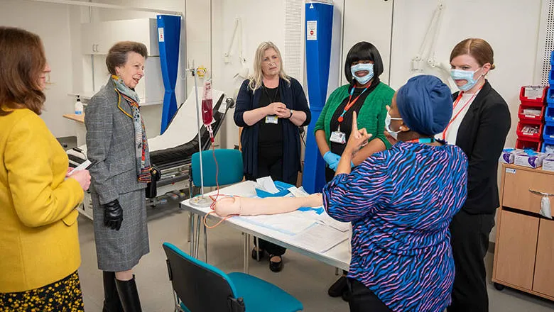 Princess Anne with group of students and staff standing over a table with a clinical simulation prosthetic arm