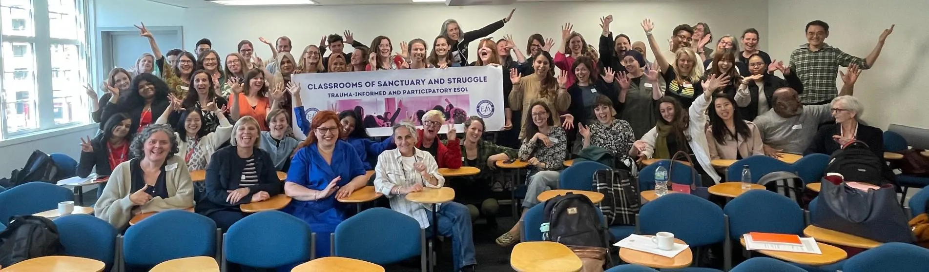 Teachers and students posing at the end of a class of English for speakers of other language, with a banner 'Classrooms of sanctuary and struggle'.