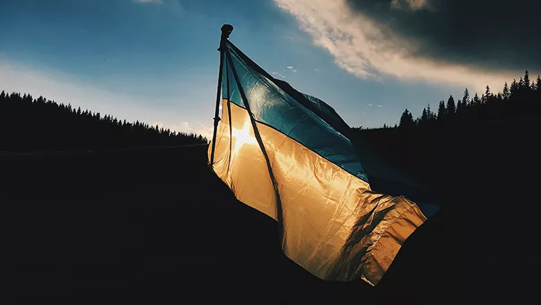 Ukraine flag flying in front of silhouetted landscape and dark skies