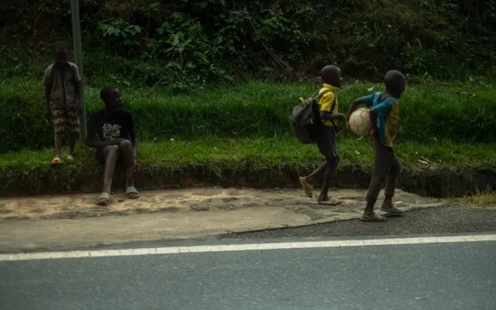 4 teenage boys on a road in Rwanda, two sitting, two walking holding a football. 