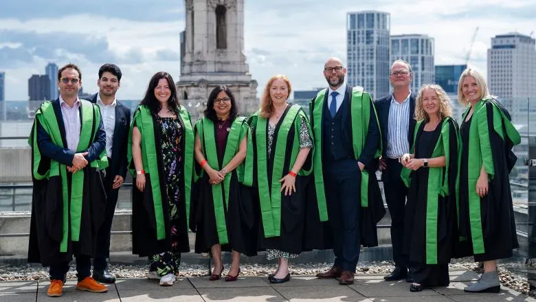 Members of the EMBA 2025 cohort of graduates pose on the roof terrace of a tall building