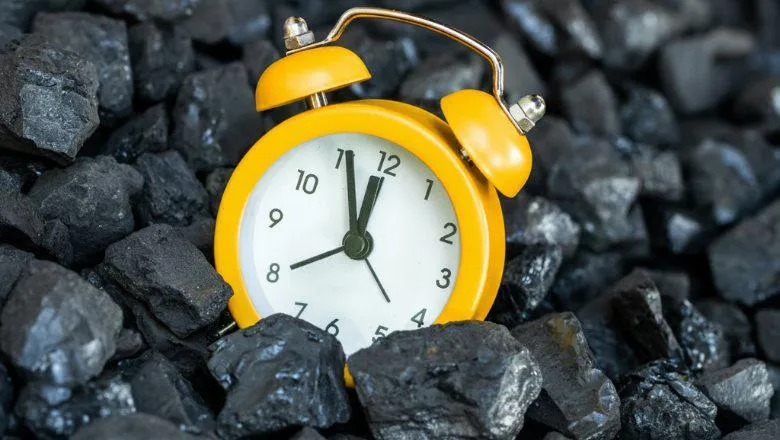A yellow alarm clock on a bed of coal