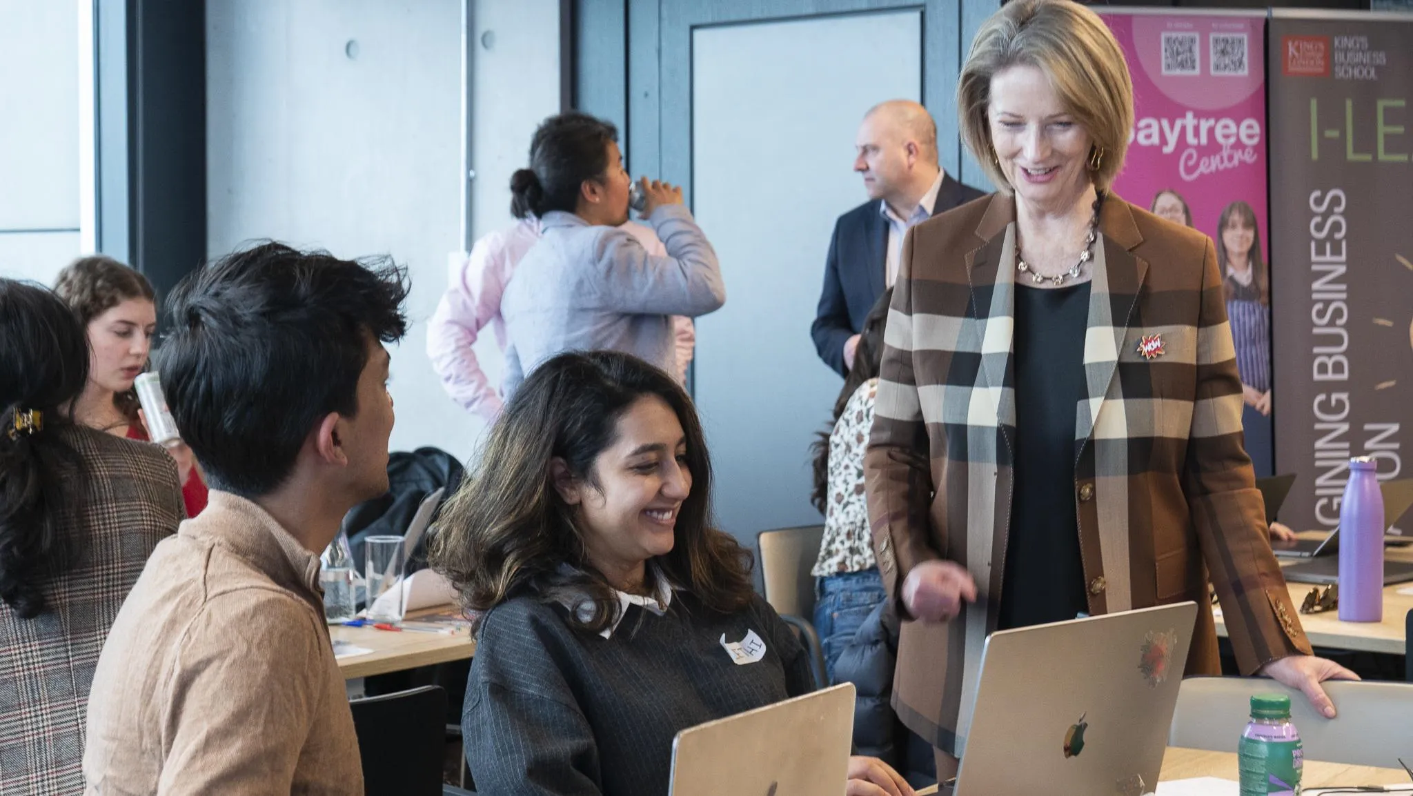 two young people working on laptops chat with Julia Gillard