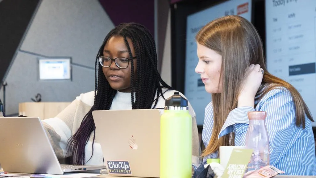 two young women look at a laptop screen as they discuss their work