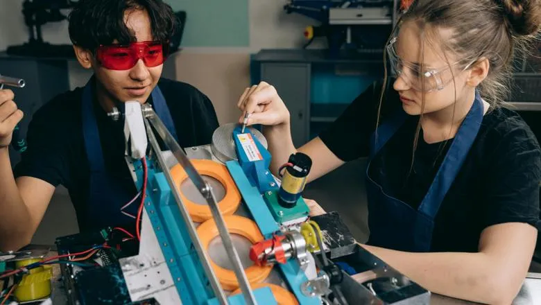 two young students wearing safety googles practice working on a machine