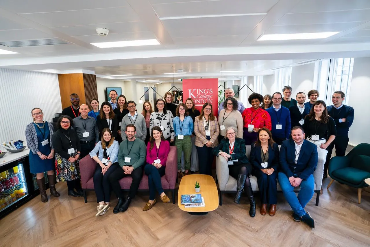 a group of around thirty people pose for a photo, the red King's logo is on the wall behind them