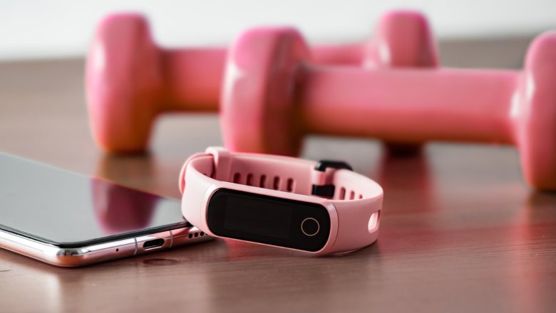 Fitness tracker on smartphone and pink colored dumb-bell on wooden tabletop
