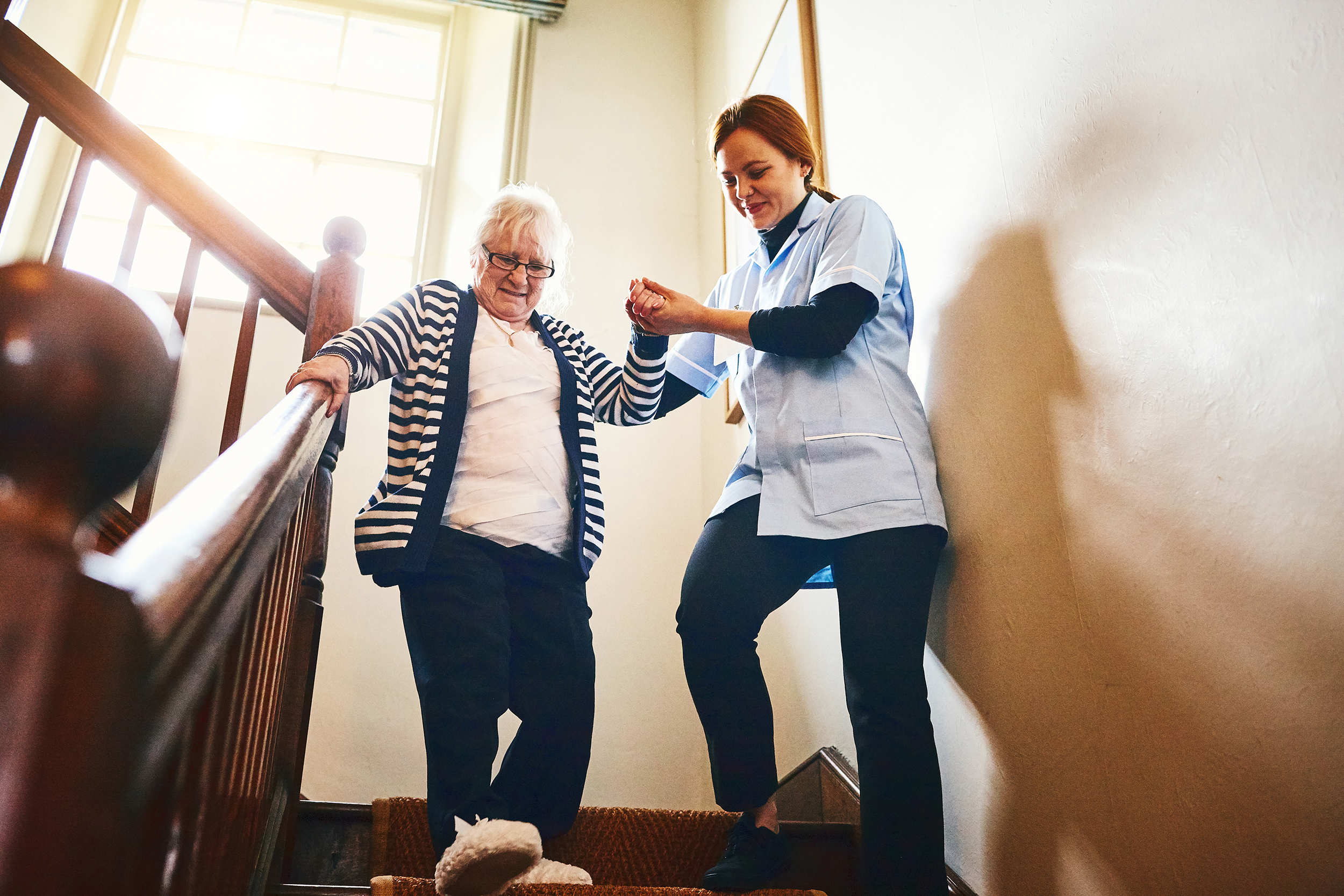 Image of Nurse Helping Senior Down Wooden Stairs