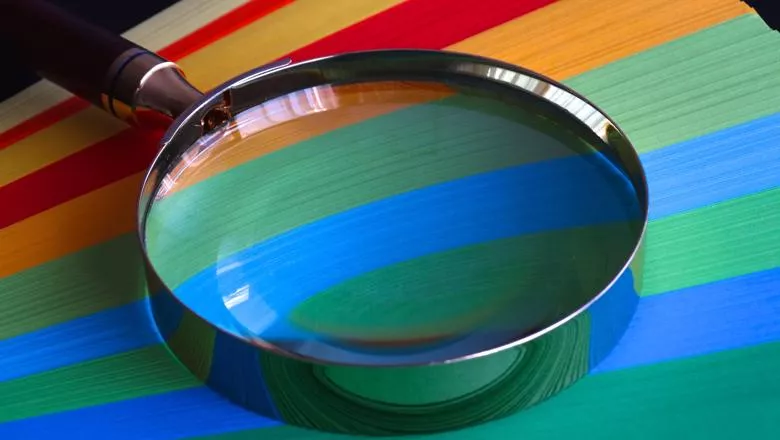 A magnifying glass against a stack of coloured paper