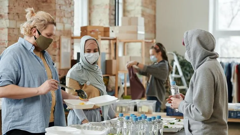 Woman in hijab and man both wearing masks serving food. Photo by Julia M Cameron from Pexels