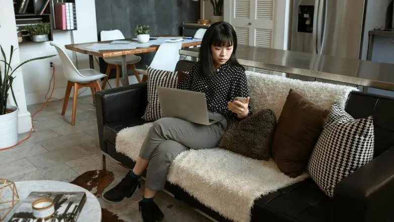 Woman Looking At Her Cellphone While Using Laptop