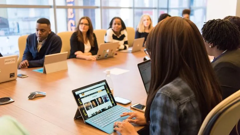 A group of diverse people sitting at a table with their computers open. 