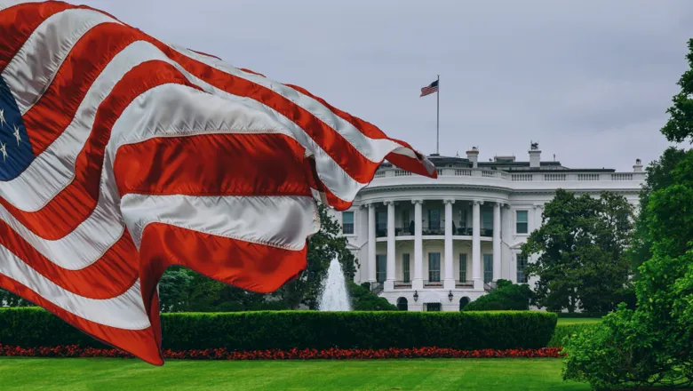 The exterior of the White House accompanied by the US flag waving in the wind.