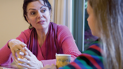 Two women conversing over a table holding coffee mugs