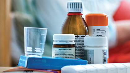 Medicines and pill box on a hospital bedside table with a patient in the background