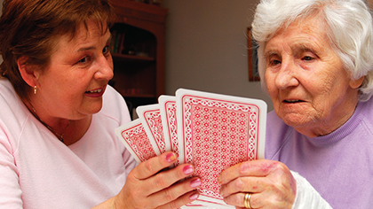 Elderly patient and her female carer playing a game with a large-print pack of cards