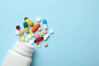 White pill bottle spilling out varying medical drugs on a blue background
