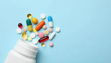 White pill bottle spilling out varying medical drugs on a blue background
