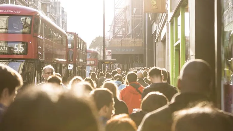 A busy street in central London, with lots of people walking and a queue of buses passing