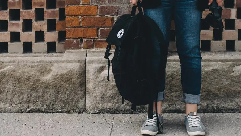 Legs and feet of young woman, holding a backpack