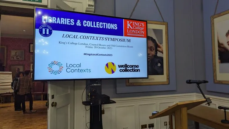 A close up of a screen in the council room for the Local Contexts Symposium, showing the name of the symposium and the dates and hosts