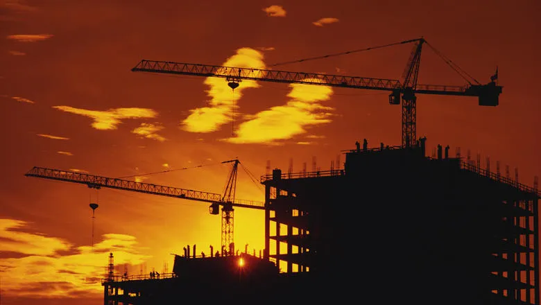 cranes and a building in construction are silhouetted against a deep orange and amber sunset. 