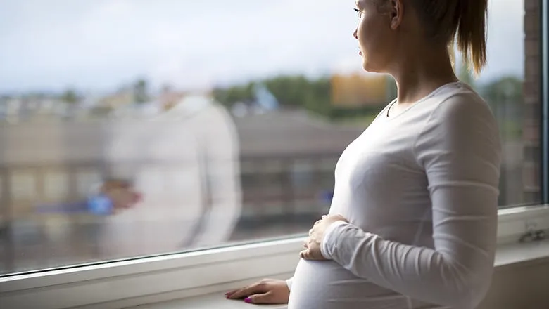 Woman in white top with hand on her belly looks out of the window