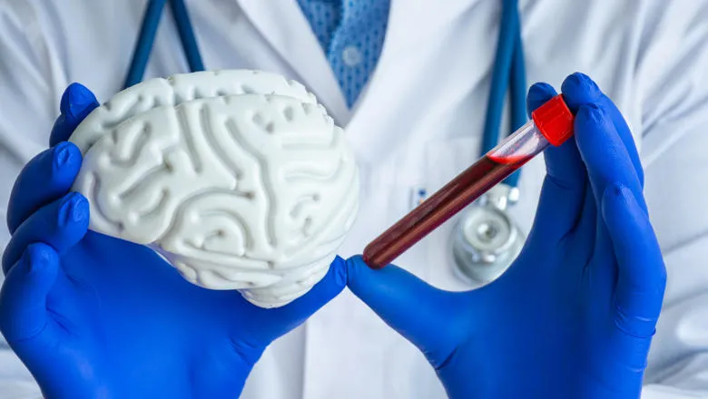 A scientist holding a model of a brain and a test tube of blood.