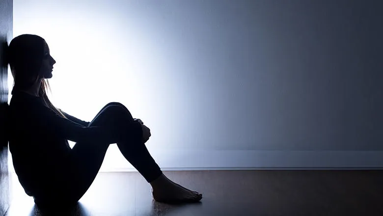Girl sitting in a dark room with arms round her legs