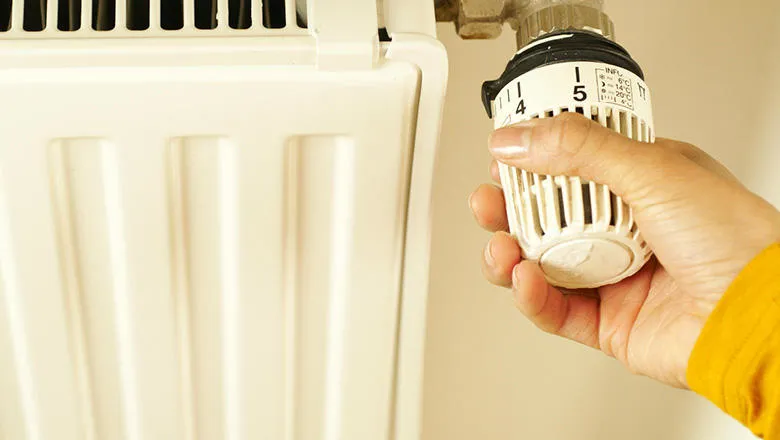 A hand turning a Thermostatic Radiator Valve on a radiator