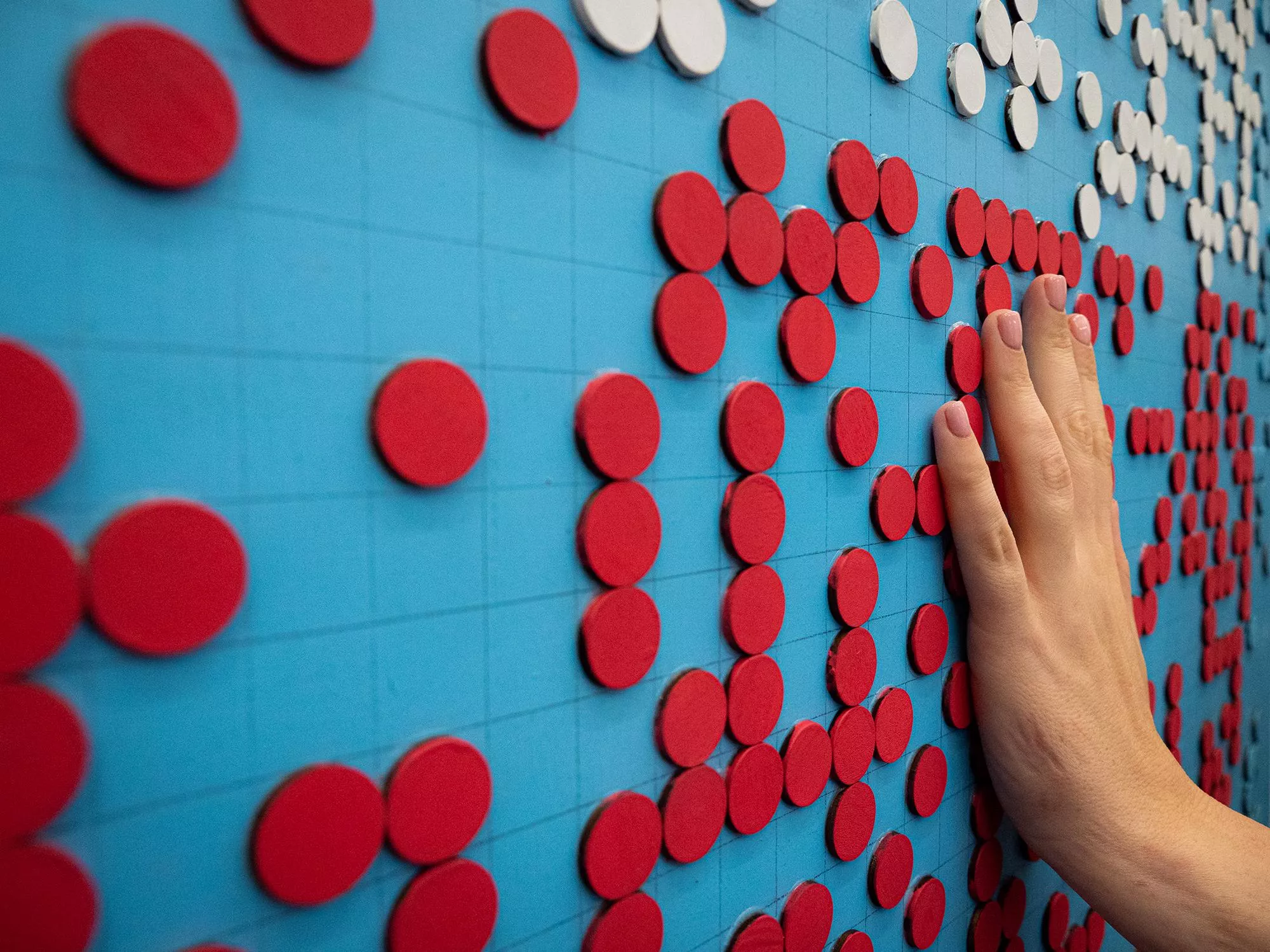 A hand touches an artwork called Fab Lolly with raised dots in braille.
