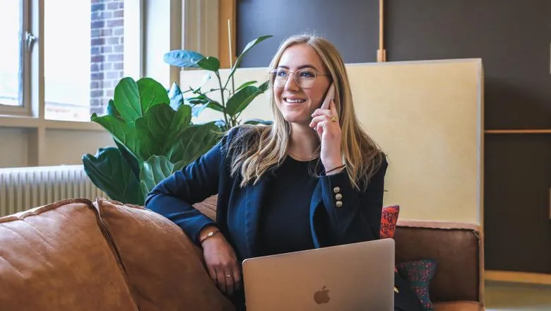 Woman entrepreneur on phone and laptop sitting on sofa