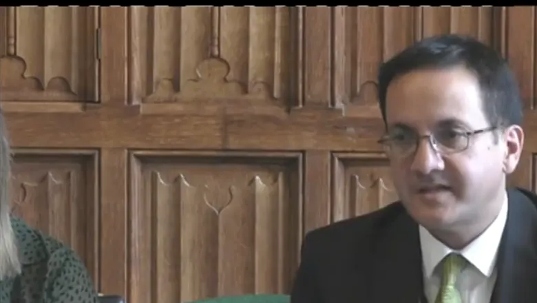Kim Hoque, wearing a suit and green tie, speaks in a parliamentary committee room