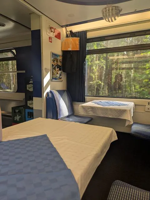 Interior of a train carriage with blue and white seating and tables, sunlight streaming through the window