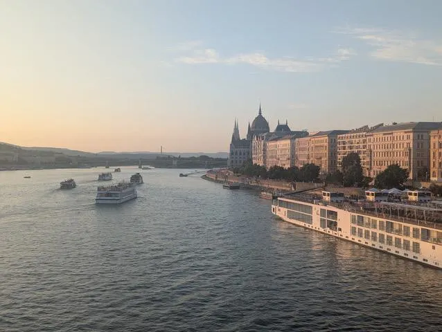 View of a river at sunset with boats and a grand domed building along the riverside.