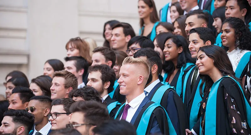 Smiling students in graduation gowns posing for photographs at graduation.