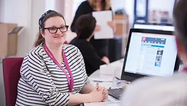 A woman sitting at a desk talking to a colleague.