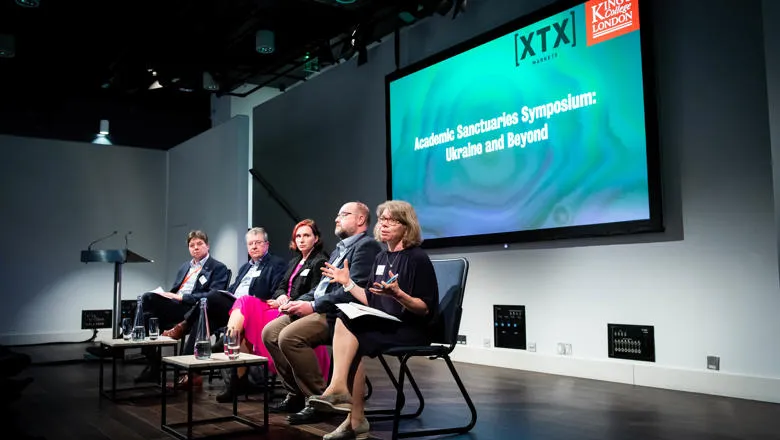 Five panelists sitting on a stage, taking part in a discussion for an academic sypmosium