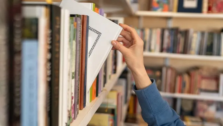 The image shows a hand pulling a book from a bookshelf in a library.