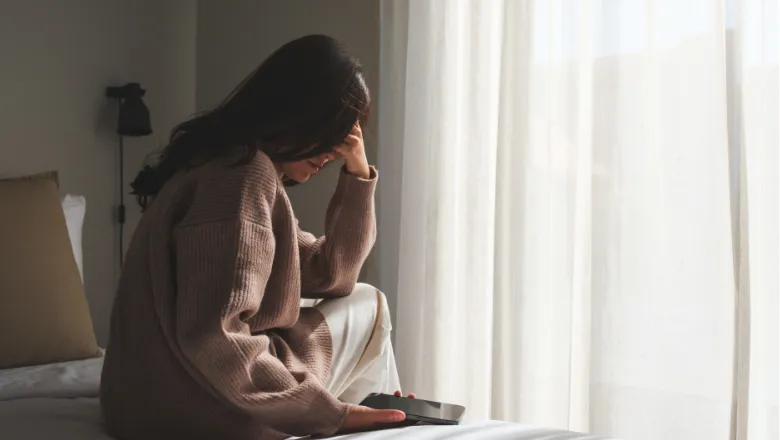 Woman covering her face in sadness while holding a phone