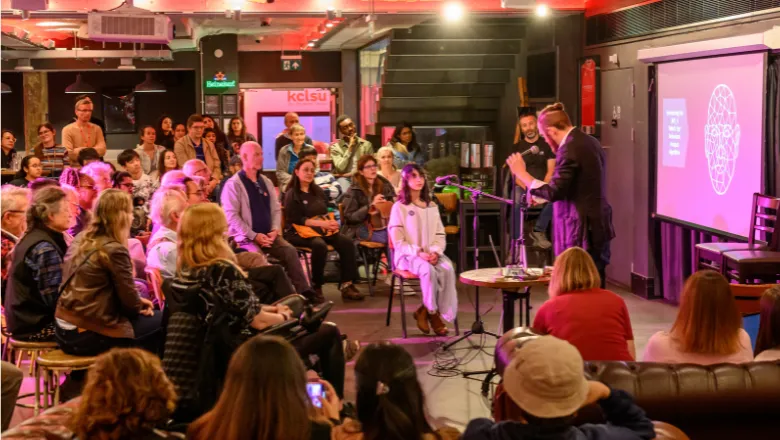 Dr Matt Tompkins and a volunteer from the audience demonstrating a magic trick at the Magic Minds and the Mysteries of AI event
