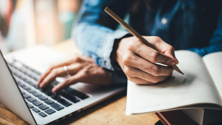 A person using a laptop and writing in a notebook.