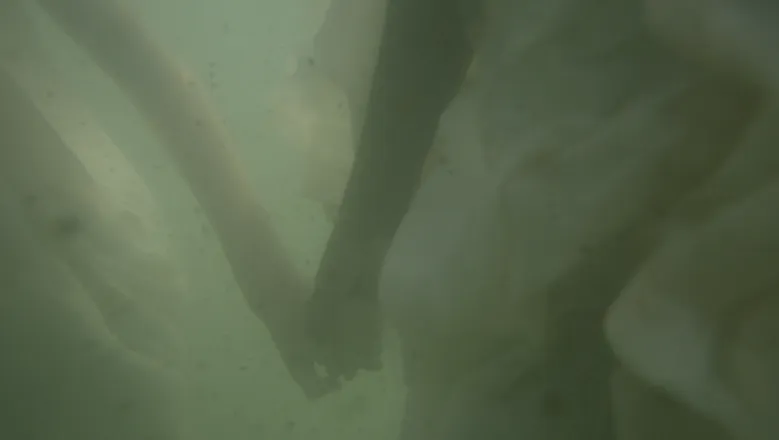 The image shows two people holding hands underwater.