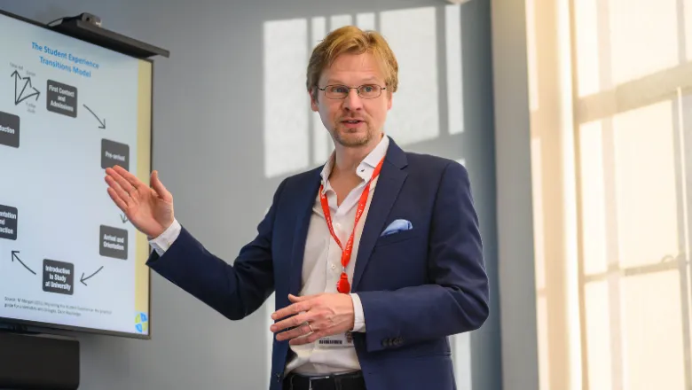 The image shows Dr Stefan Bauer during a lecture at King's College London.