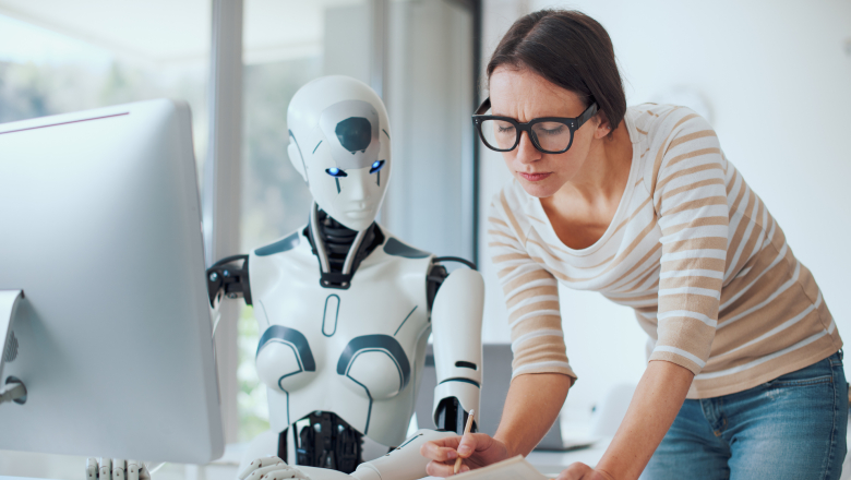 A woman in glasses holding a pencil and paper consults with a robot.